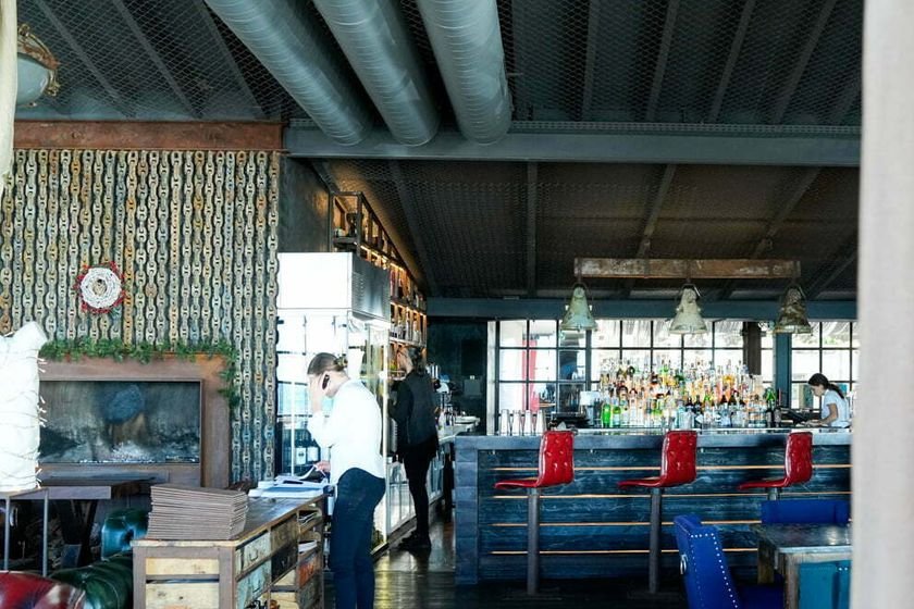 Barra de la sala al fondo, con sofá chéster granate y sillas de terciopelo azul en primer plano.