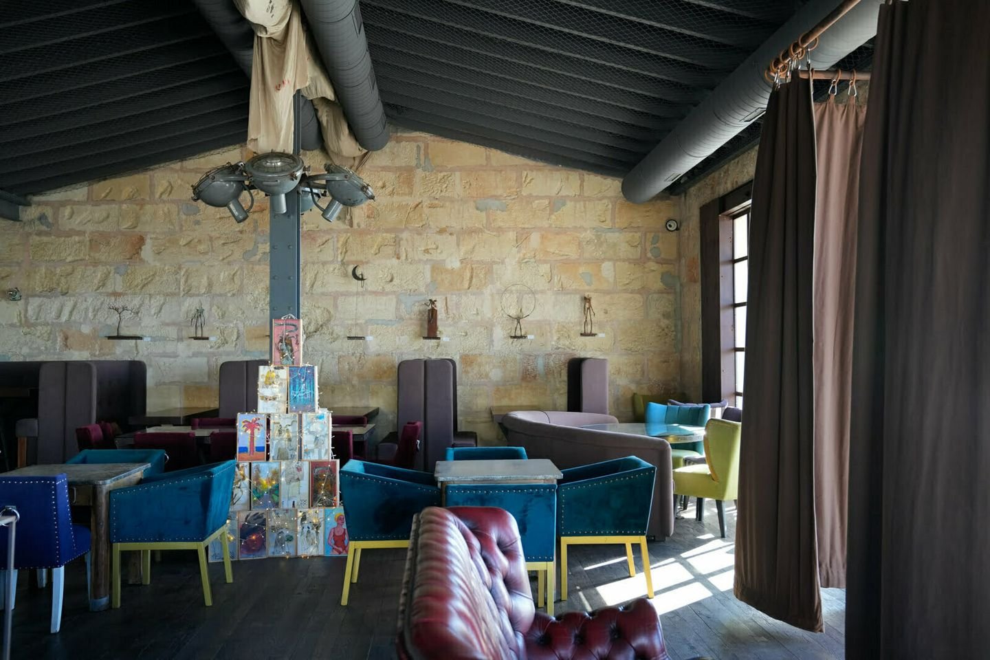 Sala con muro de piedra de marés, techo de acero negro y butacas de terciopelo azul y granate.